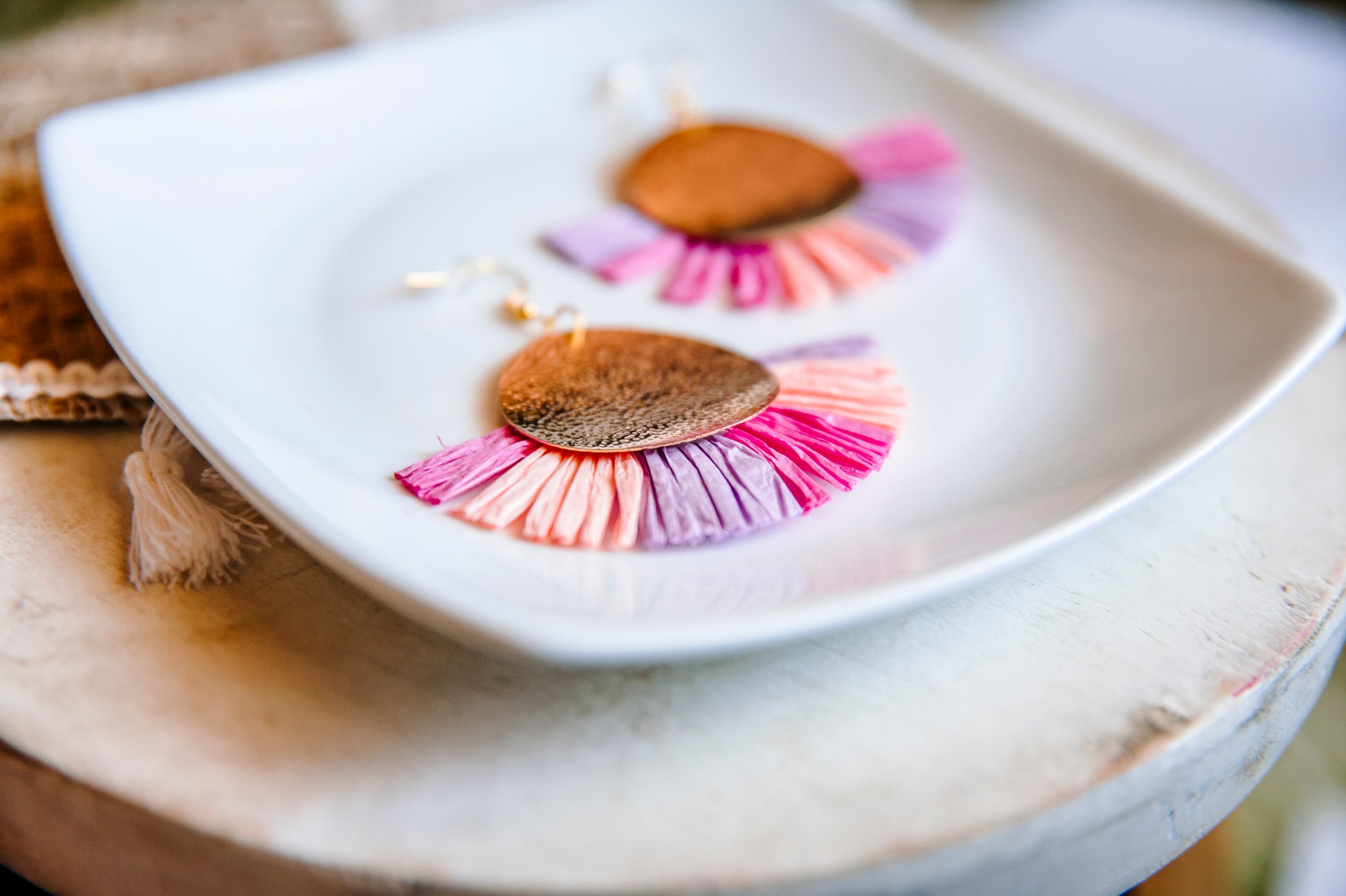 Pink, peach, and purple raffia making a fan shape half circle with a gold textured circle connected to the post. Displayed on a white plate.