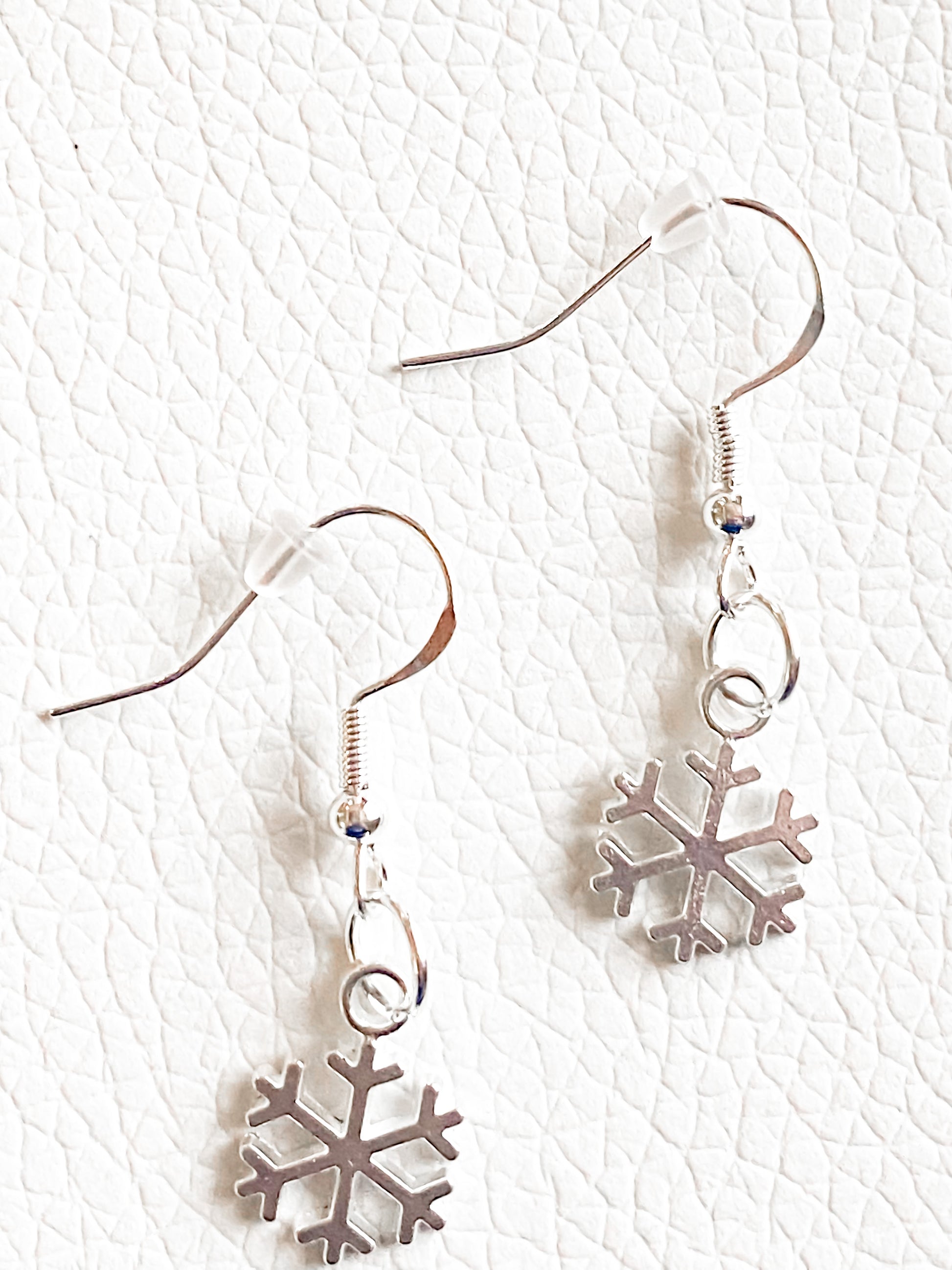 close up shot of the petite snowflake silver earrings. The hooks are silver with clear rubber backs. set against a textured white background